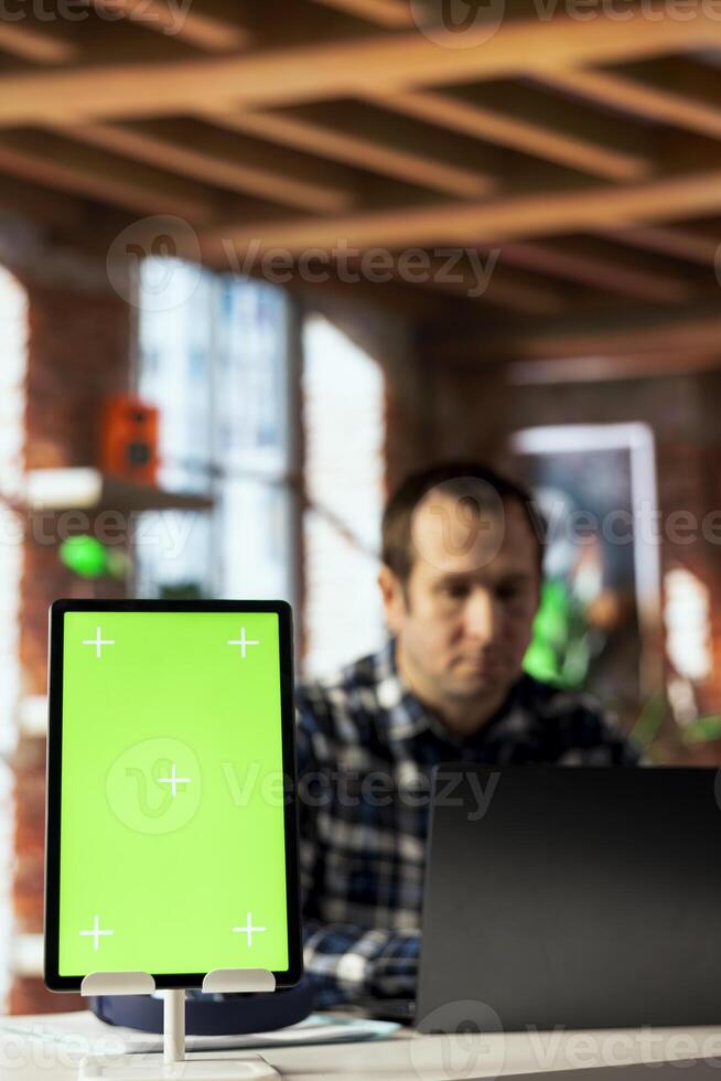 Focus on employee in blurry background using green screen tablet, preparing presentation. Close up of mockup device used by remote worker finishing business project, uploading files photo