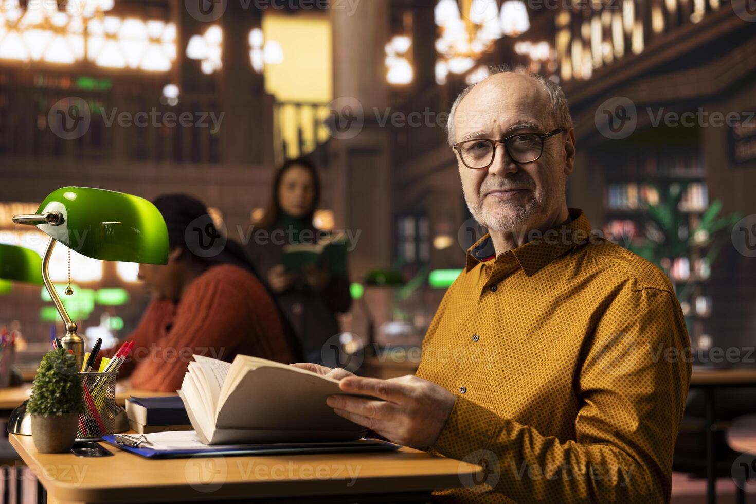 Wise aged person reading a book at the public library and enjoying free time, having a classic hobby of gaining knowledge during retirement. Happy relaxed pensioner with spectacles. photo