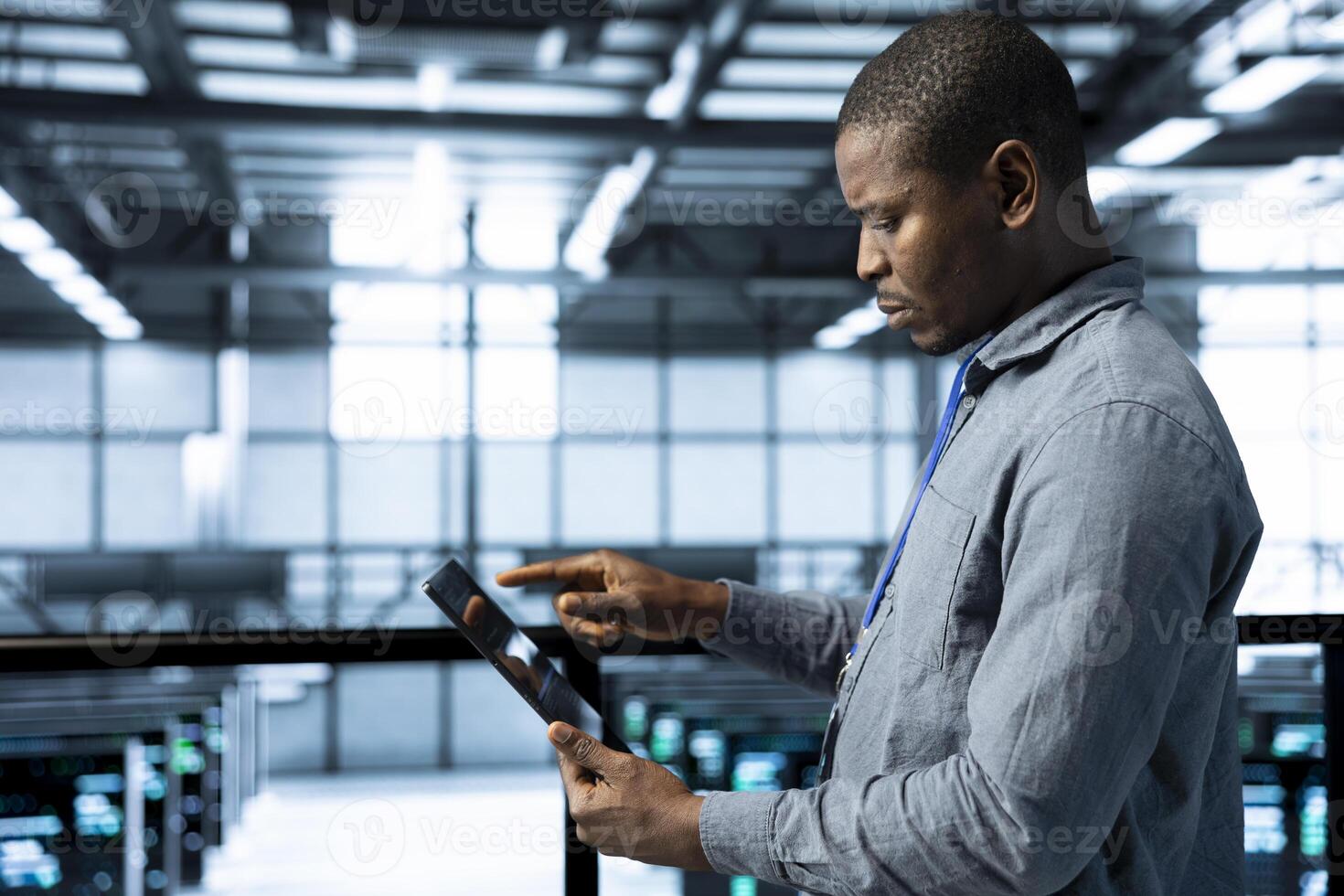 Admin in data center using tablet to deploy new server architectures, configuring network virtualization. Man in server room updating storage arrays, verifying settings to maintain stable performance photo