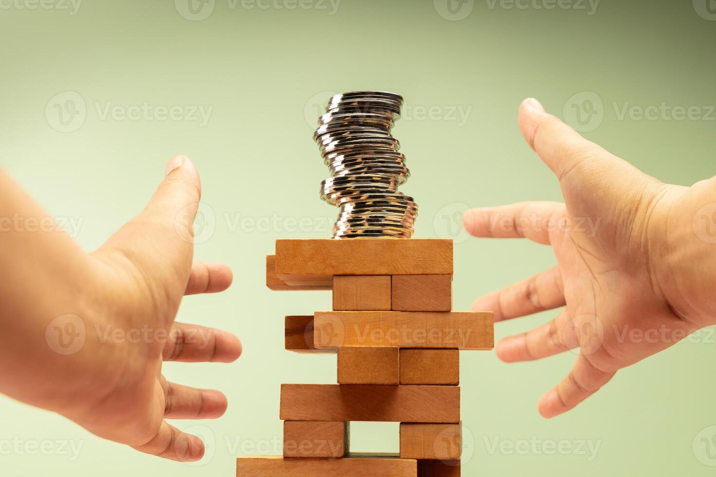 Coin Stack on precariously Jenga blocks, hands protecting it, symbolizing fragile financial stability and economic uncertainty, need for caution photo