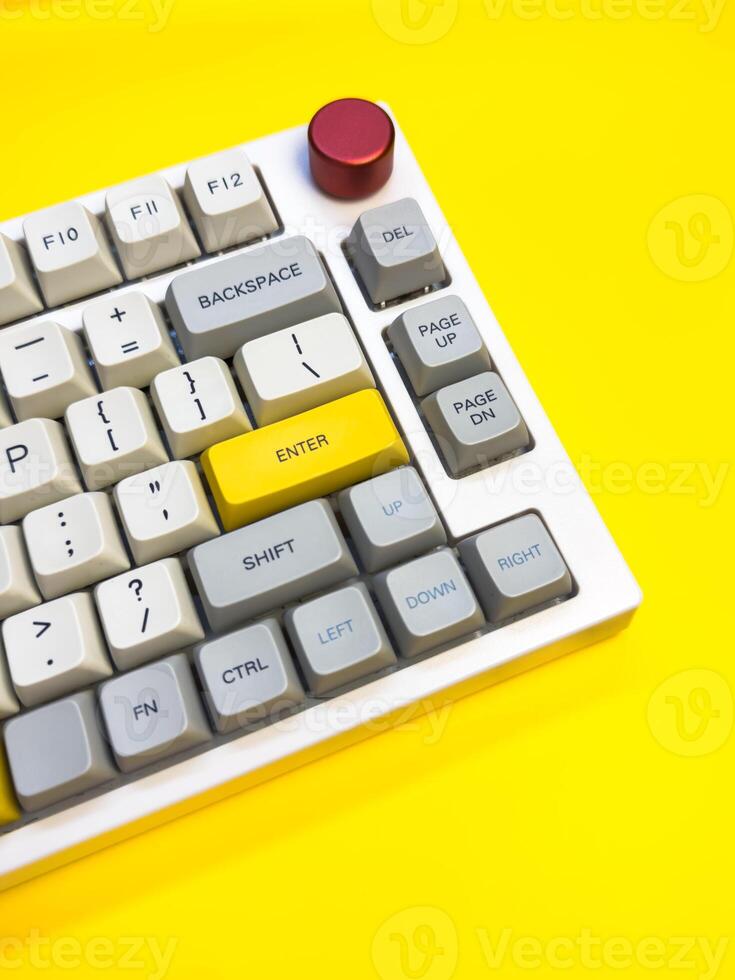 White mechanical keyboard with bright Enter key on bright yellow background, minimalism, vertical photo