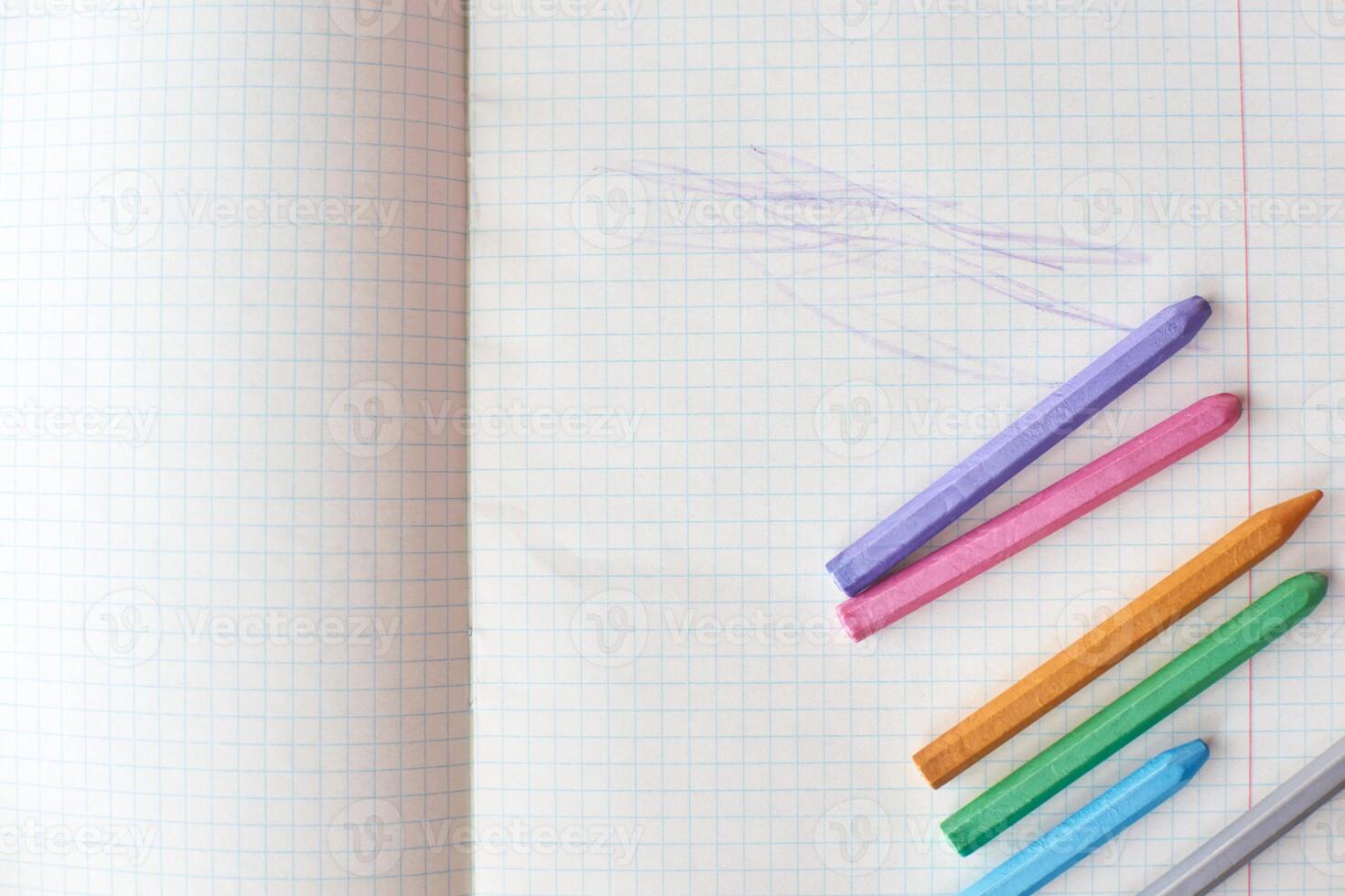 Colorful crayons lined up on opened graph paper notebook with abstract scribbles. photo