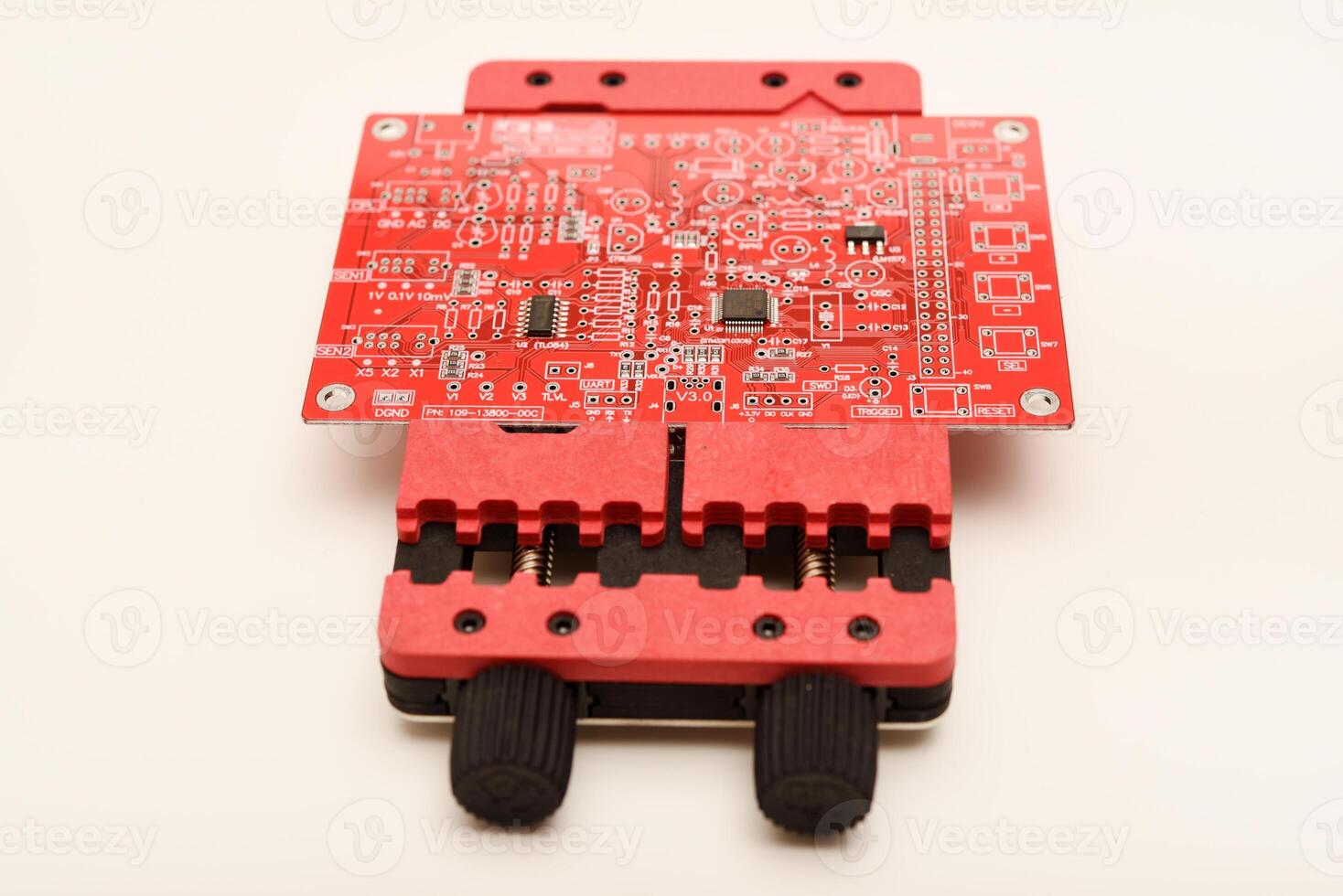 Universal electronics repair tool firmly clamping a red printed circuit board for detailed component work. photo