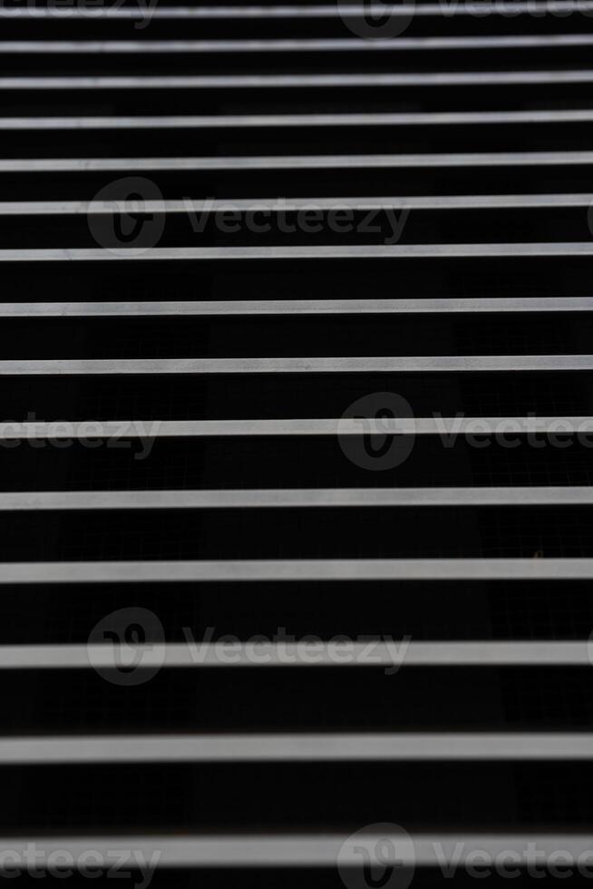 Image shows a series of evenly spaced horizontal metal bars against a dark background, creating a repetitive linear pattern. Suitable for illustrating concepts of structure, security, or industrial design in visual projects. photo
