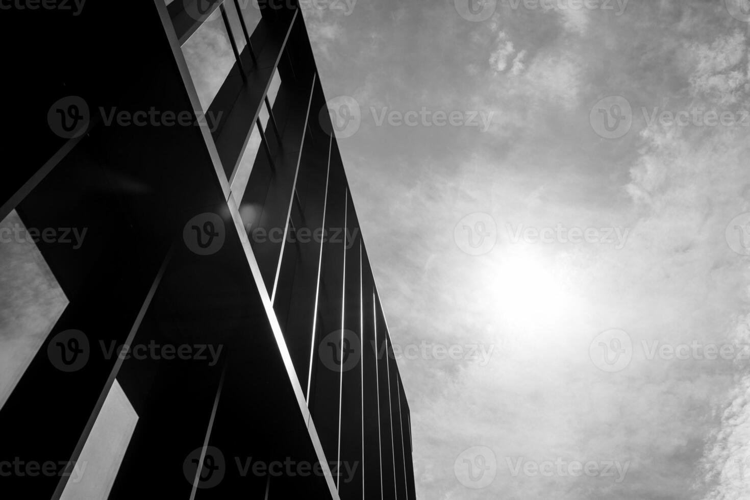 Black and white photo of a modern building facade with strong vertical lines and sunlight in a cloudy sky. Suitable for illustrating architecture, urban design, or minimalism concepts in editorial and commercial projects.
