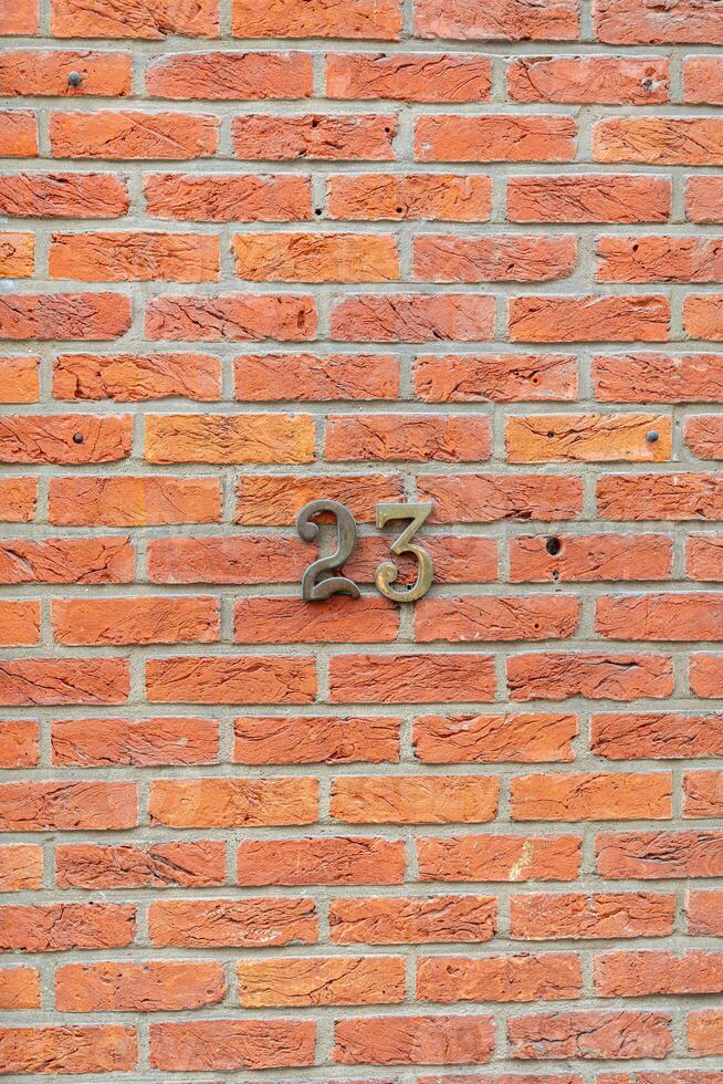 Metal house number twenty three fixed on a red brick wall indicating the address of a building, providing information and guidance for visitors and residents, photo