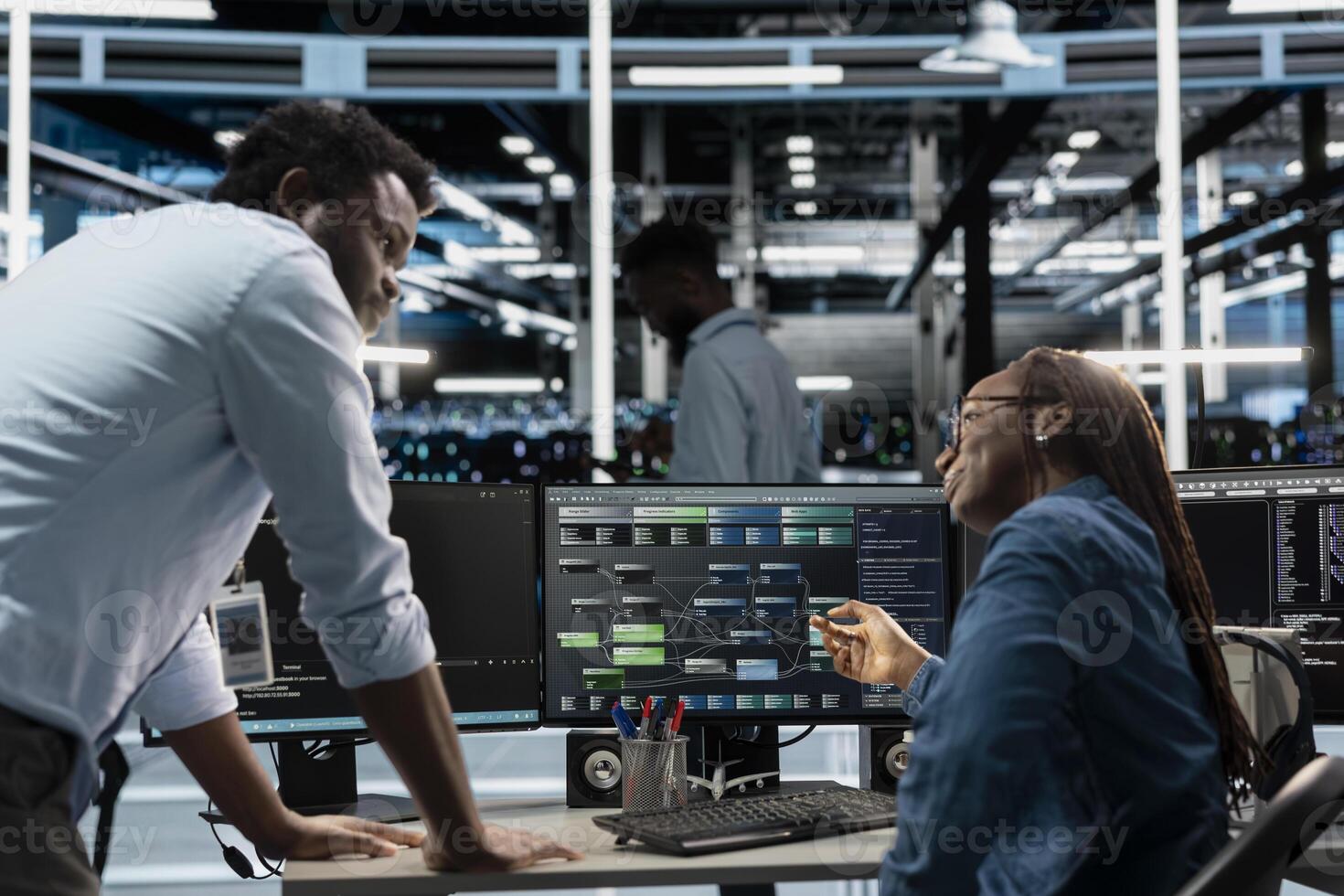 Supervisor checking work done by engineer programming in server hub housing infrastructure storing datasets. African american team leader overseeing IT specialist repairing data center racks photo
