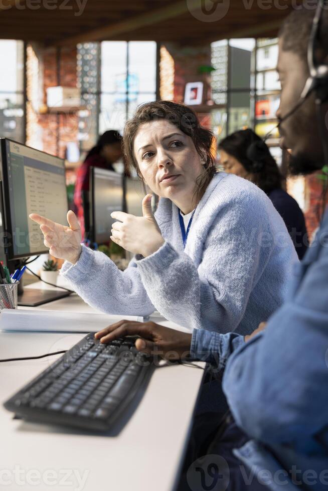 Customer service manager supervising man logging customer interactions in CSM system on computer. Call center supervisor overseeing employee using customer service management software on PC photo