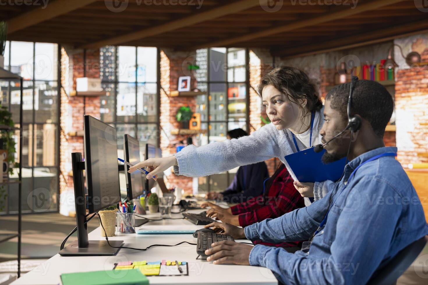 Customer service manager teaching new worker how to track support tickets in dedicated company software on computer. Call center supervisor shows african american intern how to create support tickets photo