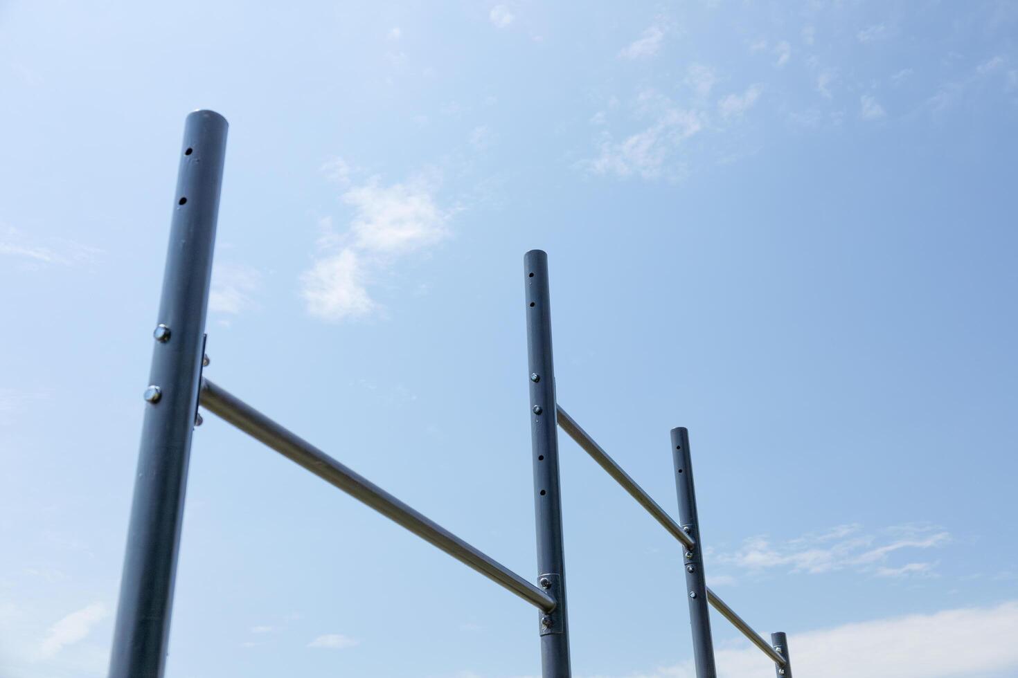 Vertical bars create a workout station for users in a serene park setting under a bright sky with few clouds photo