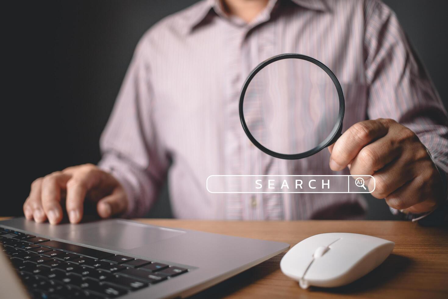 A person uses a magnifying glass near a laptop with a digital search bar overlay, symbolizing search engine optimization, focus, and the pursuit of information in a digital environment. photo