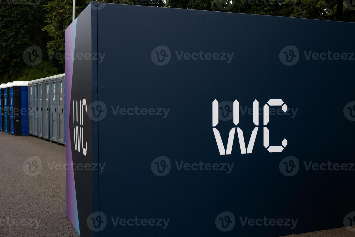 Close-up view of portable toilet with WC sign on a dark blue panel. Several portable restrooms are lined up in a row. Outdoor facilities for public use in urban or event settings photo