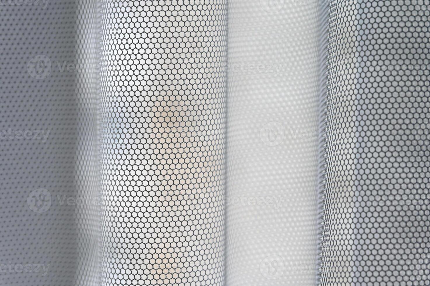 A macro close-up of a white fabric with a repeating hexagonal mesh pattern. The material is shown with soft folds, creating a sense of depth and a textured, abstract visual. photo