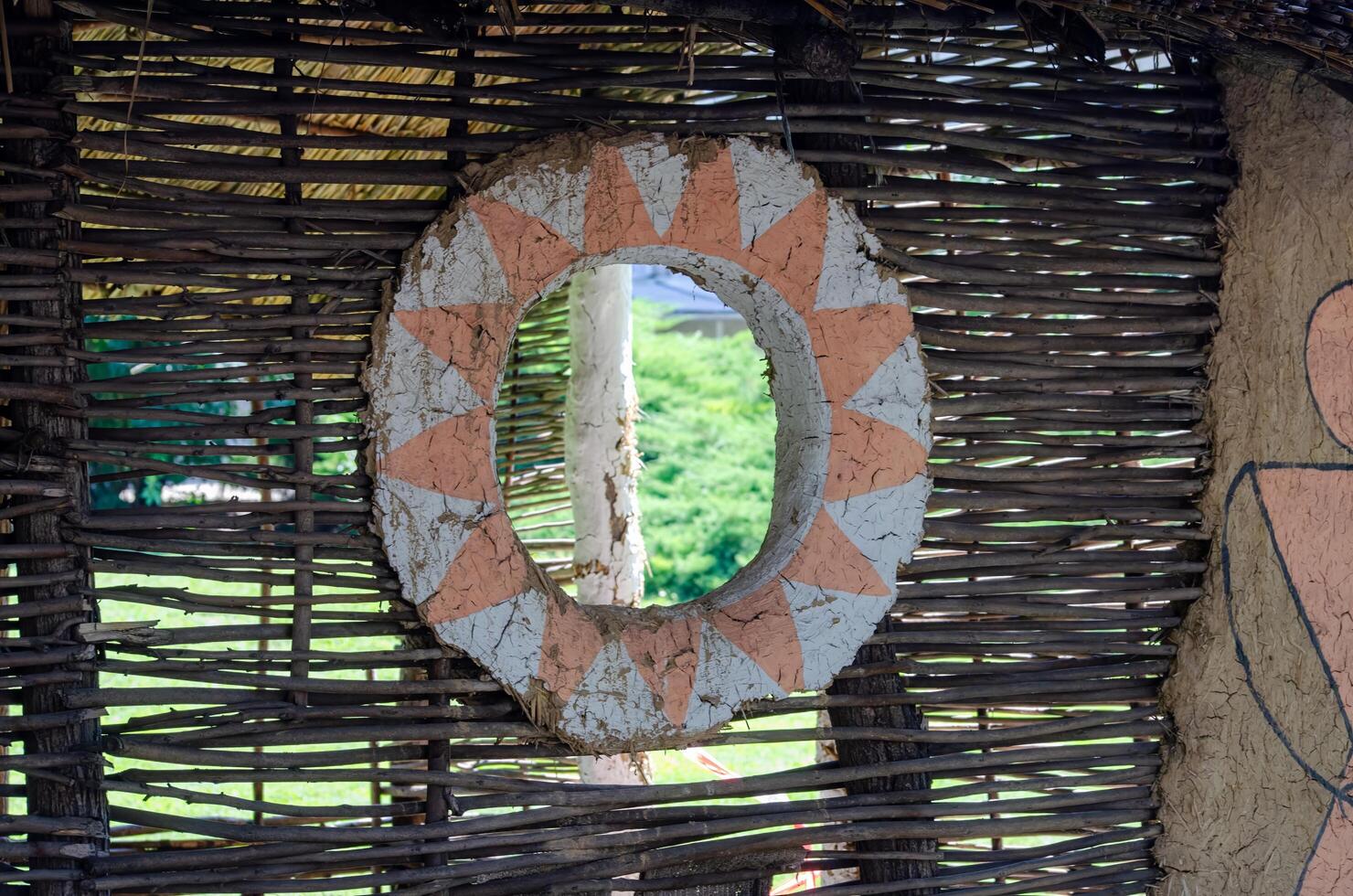 A small window with a wicker frame and a circle painted on it. The circle is surrounded by a pattern of triangles photo