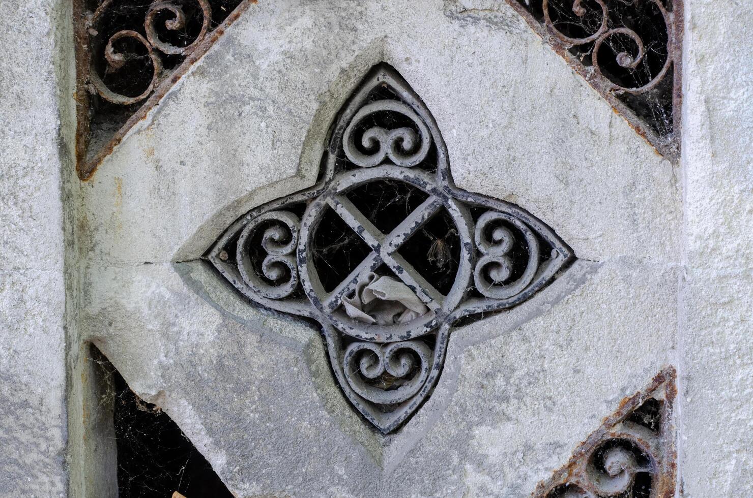 A stone carving of a cross with a spider web in the middle. The spider web is made of metal and is very detailed photo