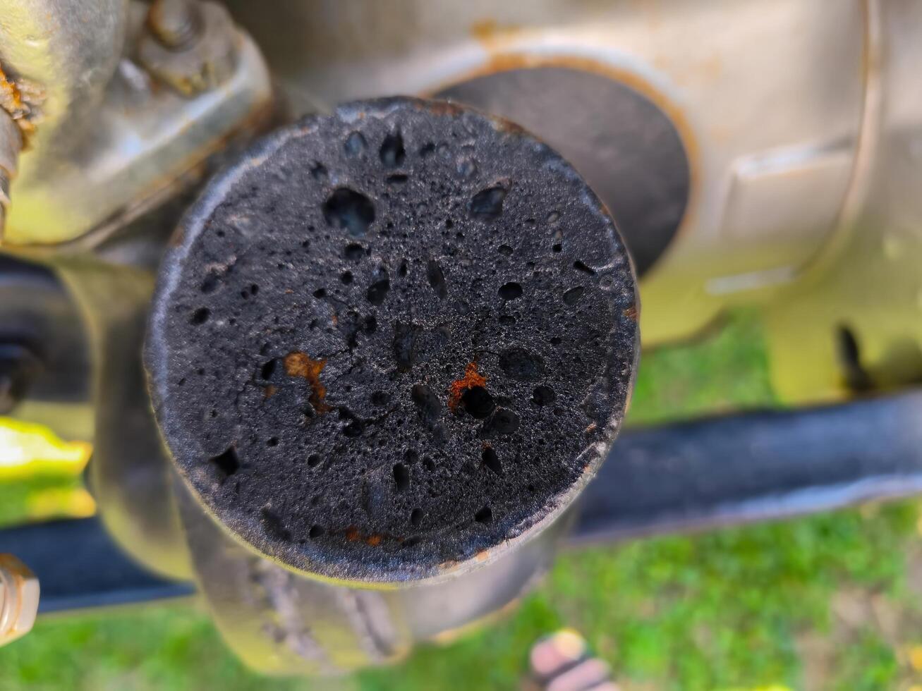 A black object with holes in it is sitting on a green grassy field. The object appears to be a piece of machinery, possibly a motorcycle, and it has been damaged. Concept of wear and tear photo
