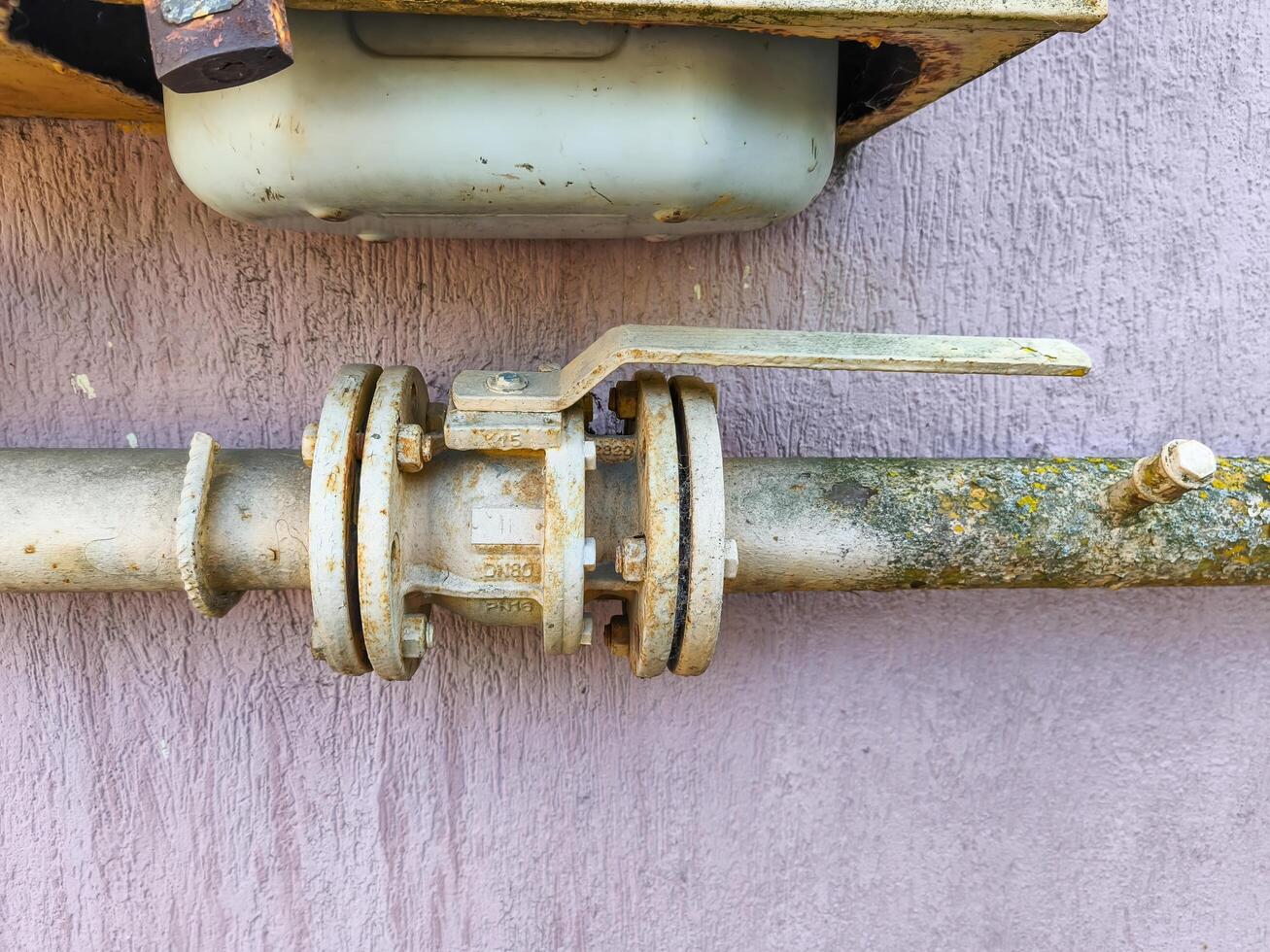 A rusty pipe with a valve on it. The valve is rusted and dirty. The pipe is old and has been exposed to the elements for a long time photo