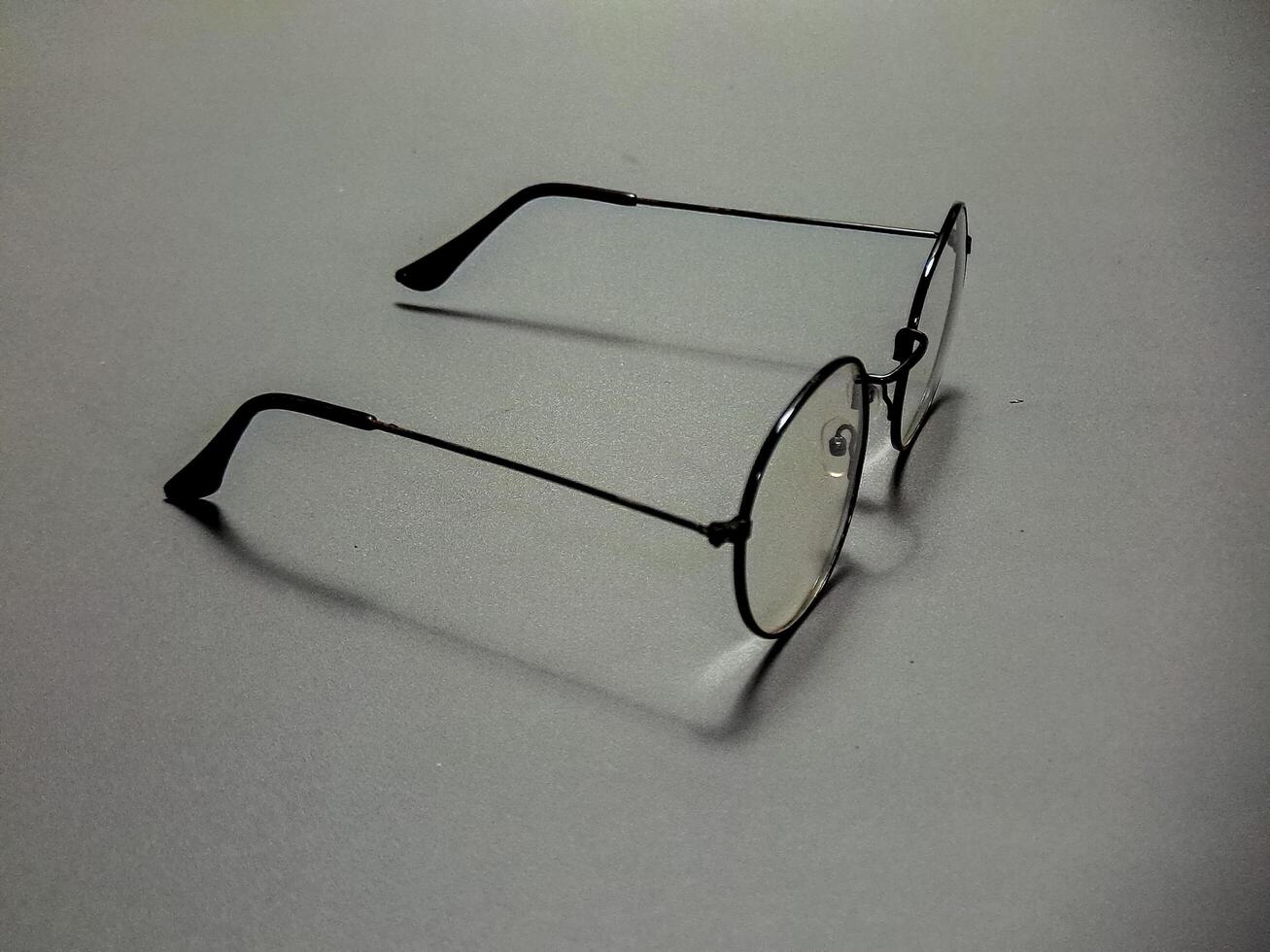 Eyeglasses with a thin black metal frame and round lenses rest on a gray surface, creating a minimalist, subtle and contemplative scene and a simple everyday style. photo