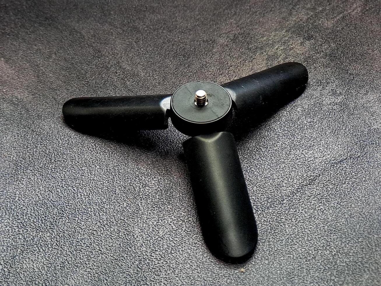Captured is a sleek, three-legged black mini-tripod situated on a textured surface, demonstrating its simple design and functionality for supporting small devices on flat surfaces. photo