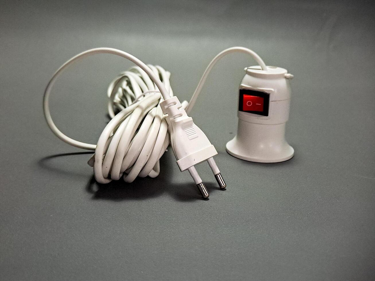 A coiled white power cord with a European plug and a socket with a red switch sits on a gray surface, creating a still life of modern electrical components, simple and functional. photo