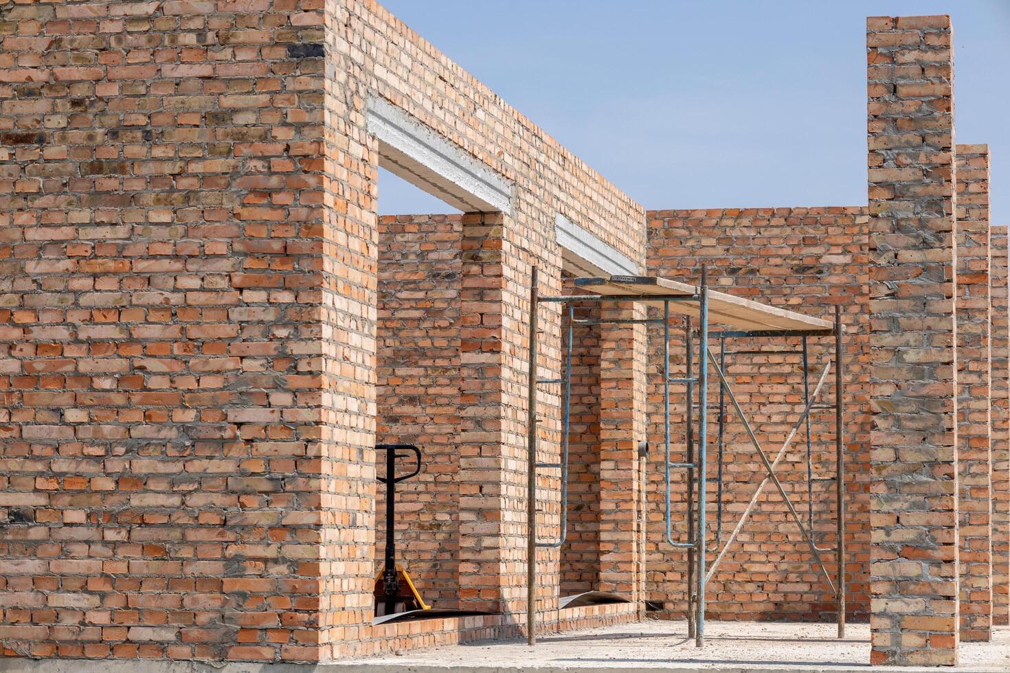 Workers are constructing a new building with brick walls and scaffolding in a bright, open area under a clear sky photo