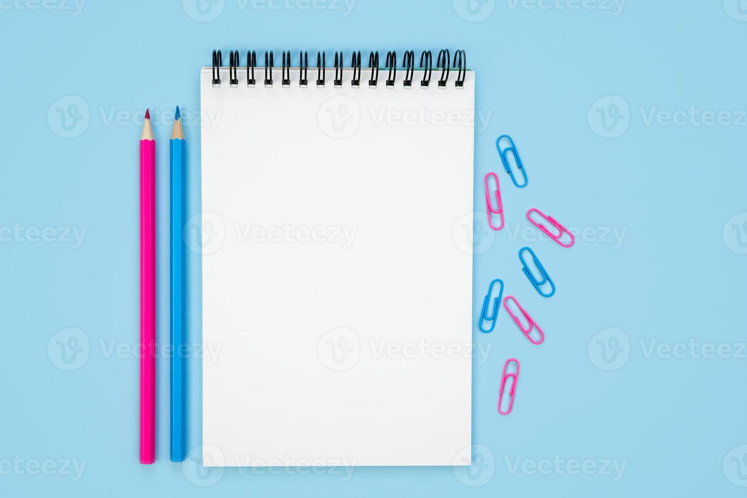 Back to school. Composition with empty notepad, pencils and paperclips on a blue background. Flatlay. Top view. Copy space. photo