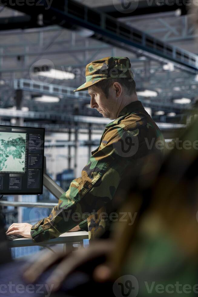 Soldier in server hub checking reports at data operations workstation monitor. Army information expert wearing uniform monitoring systems using display in operational data center photo