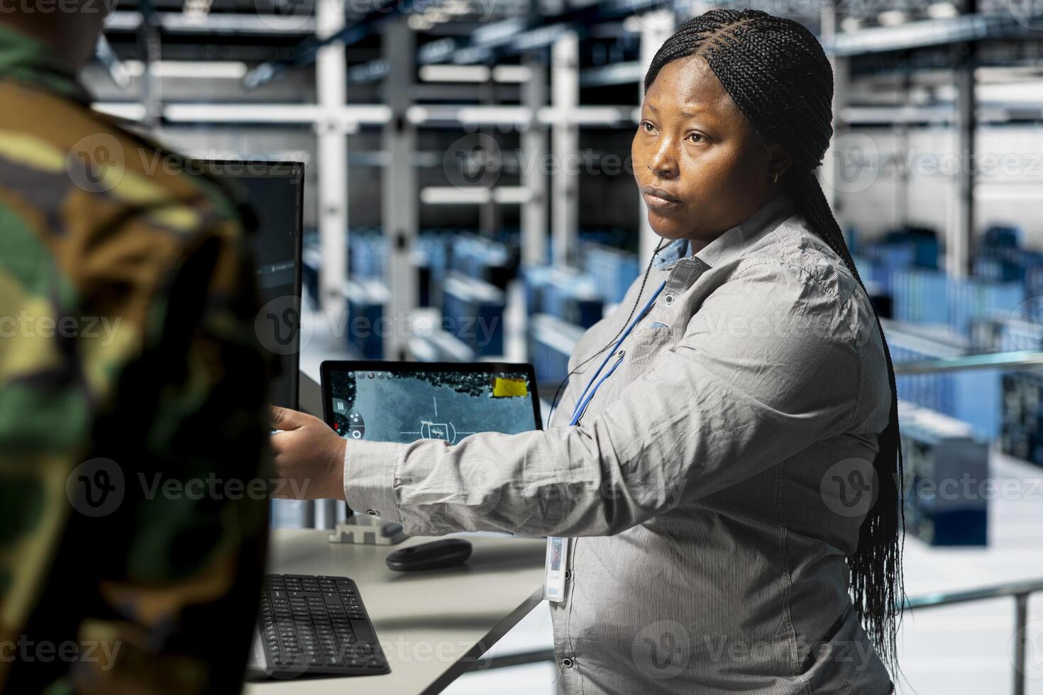 Team of soldiers in uniform confirming target locations using aerial image overlay on monitor. African american military units in server hub gathering strategic terrain data via satellite systems photo