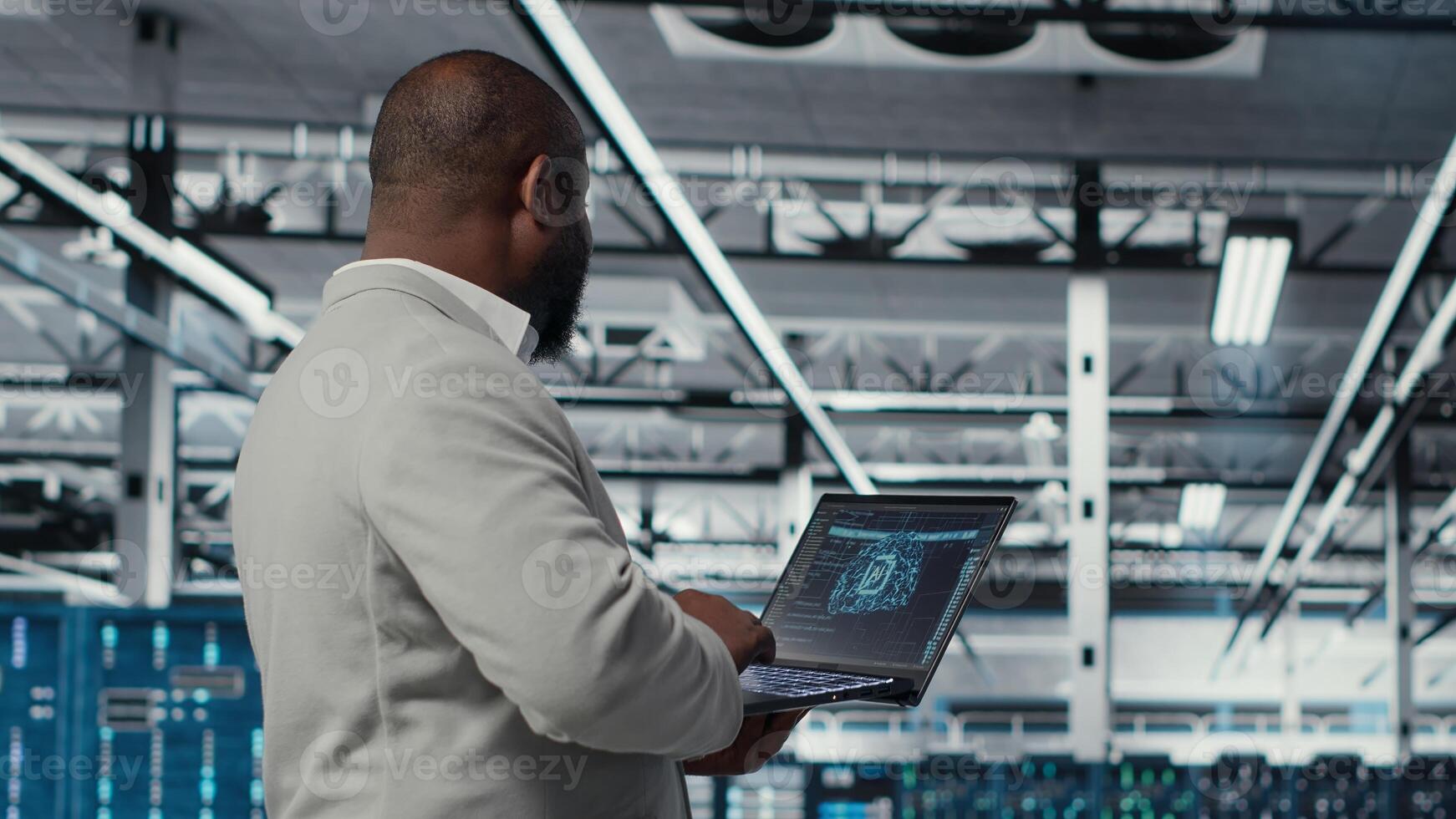 Server farm IT specialist using laptop to improve deep learning AI systems workloads. Data center software developer using notebook to adjust artificial intelligence model parameters, camera B photo