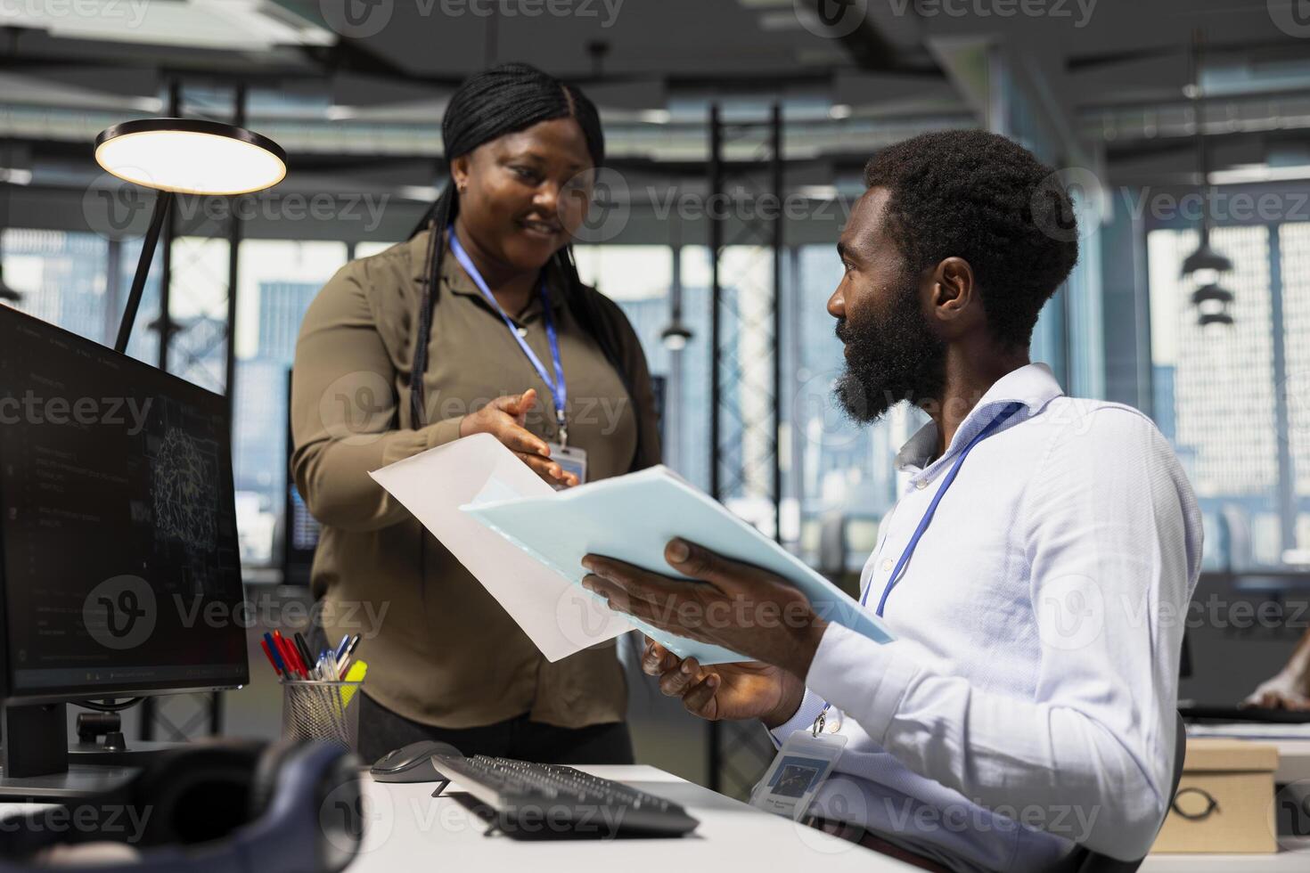 Manager in office handing paperwork to employee working with AI assistant on PC. Worker supervised by team leader while using artificial intelligence to streamline administrative tasks, camera A. photo
