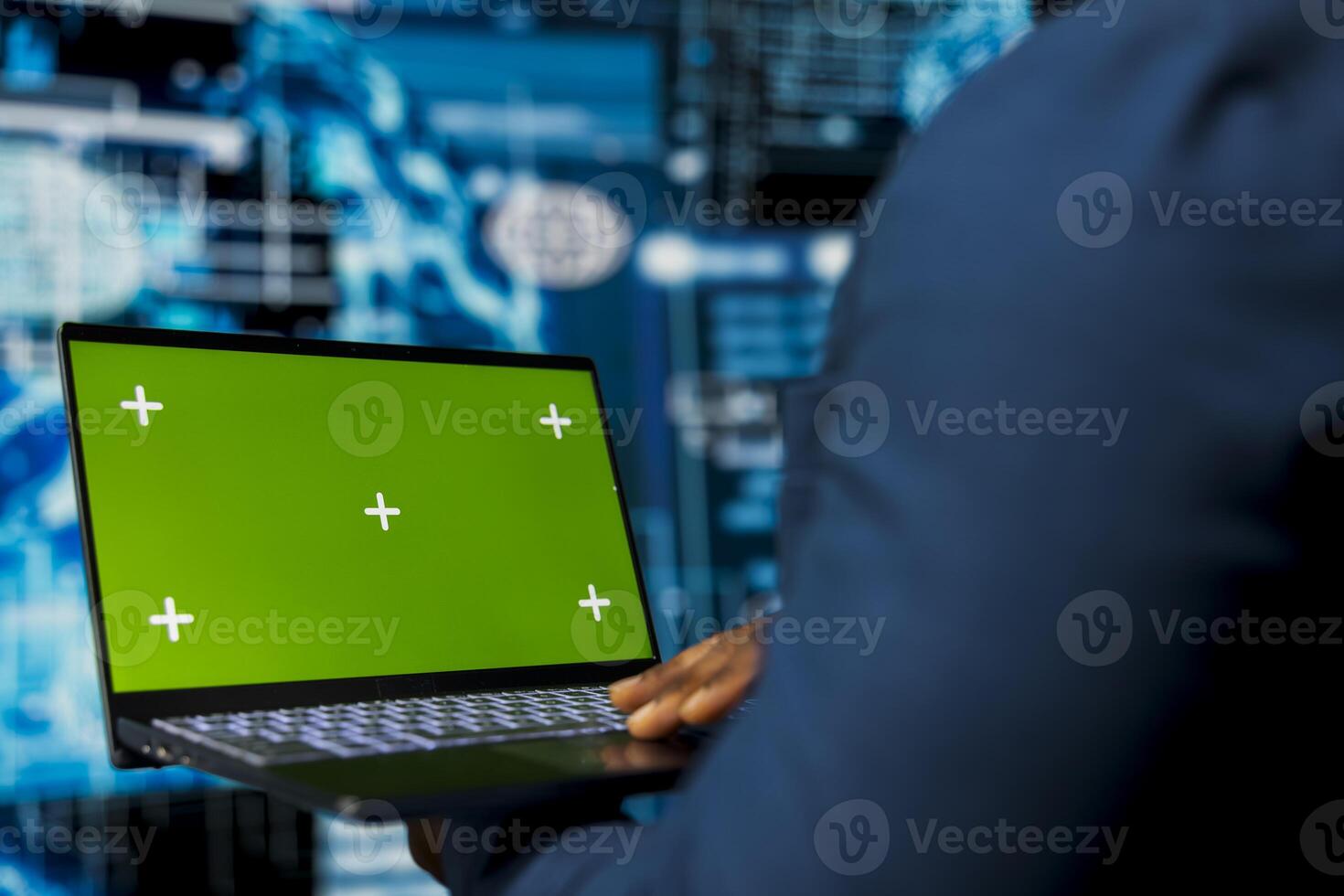 Young male specialist reviews algorithmic data next to green screen, uses laptop surrounded by digital visuals. AI smart technology and neural networks in a high tech environment. photo