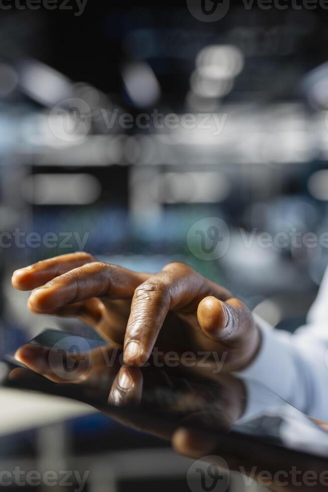 Close up of data center software developer doing maintenance tasks on tablet, ensuring optimal performance. Male worker reviewing diagnostics and debugging server hub high tech equipment. photo
