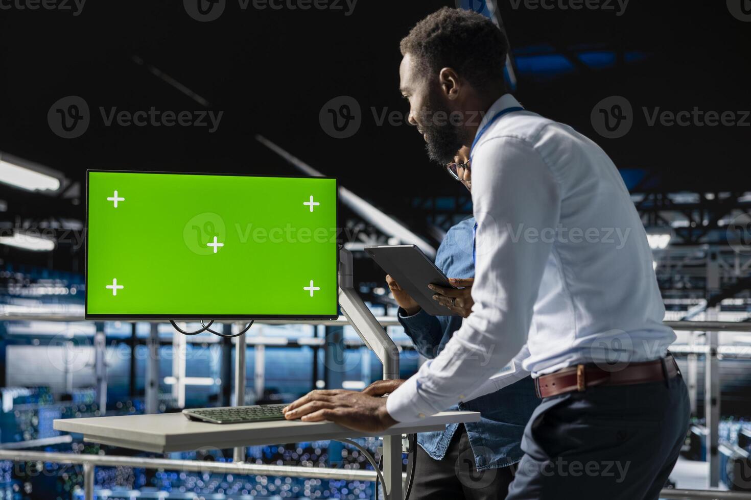 African american IT experts using chroma key device to analyze neural network systems. Data center admin uses green screen pc next to colleague, reviewing AI visualization in background. photo