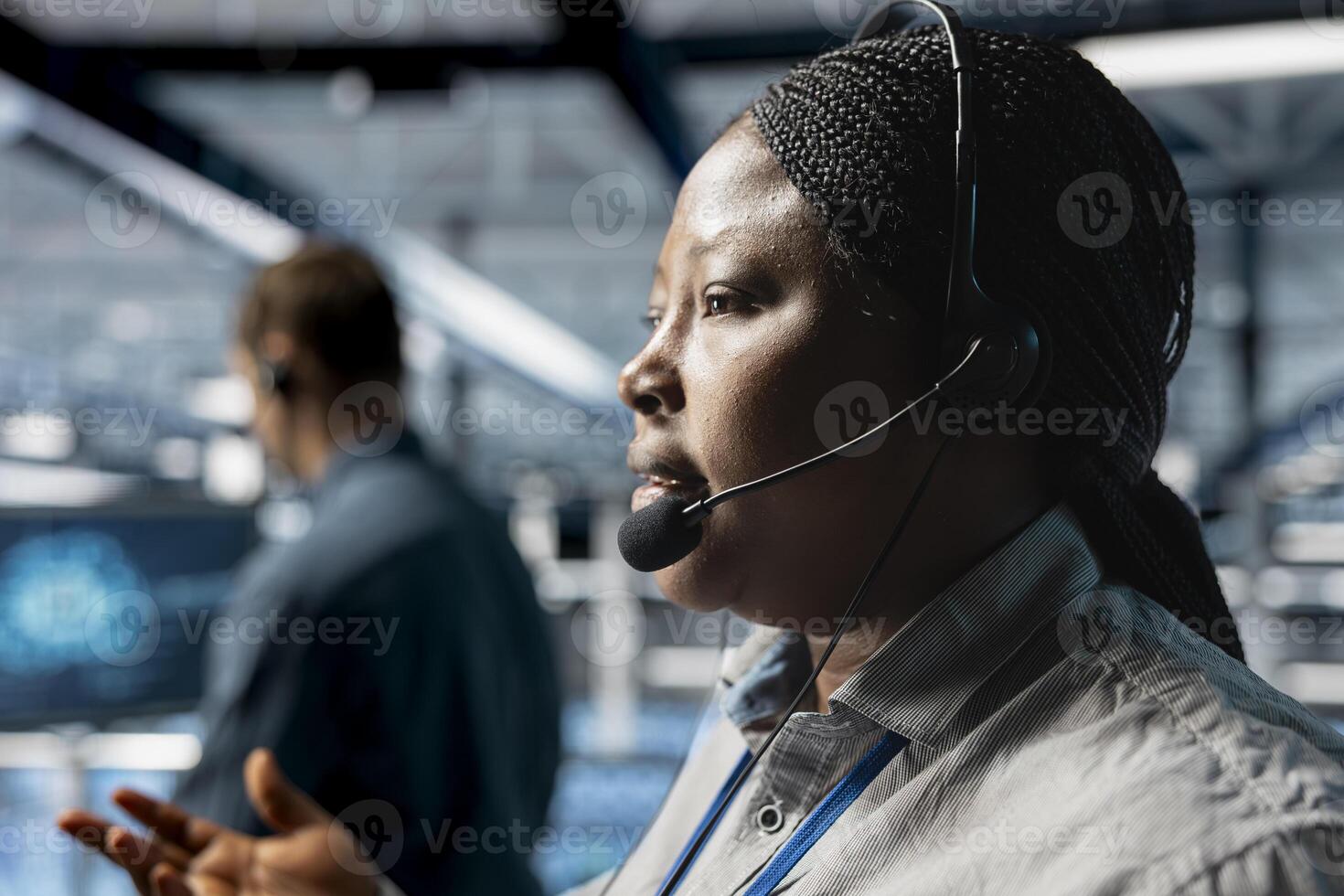 Close up of server hub coworkers escalating critical system alerts detected by AI monitoring. Data center admins walking clients through configuration steps using headset mic photo