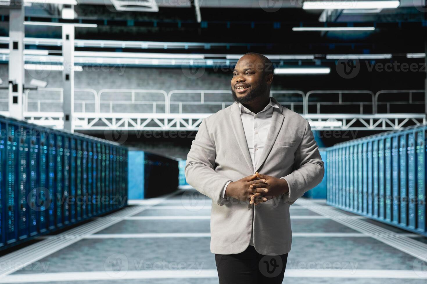 Smiling admin walking in server room, overseeing mainframes gear used for managing databases. Jolly IT specialist in data center workplace doing checkup on rackmounts storing information photo