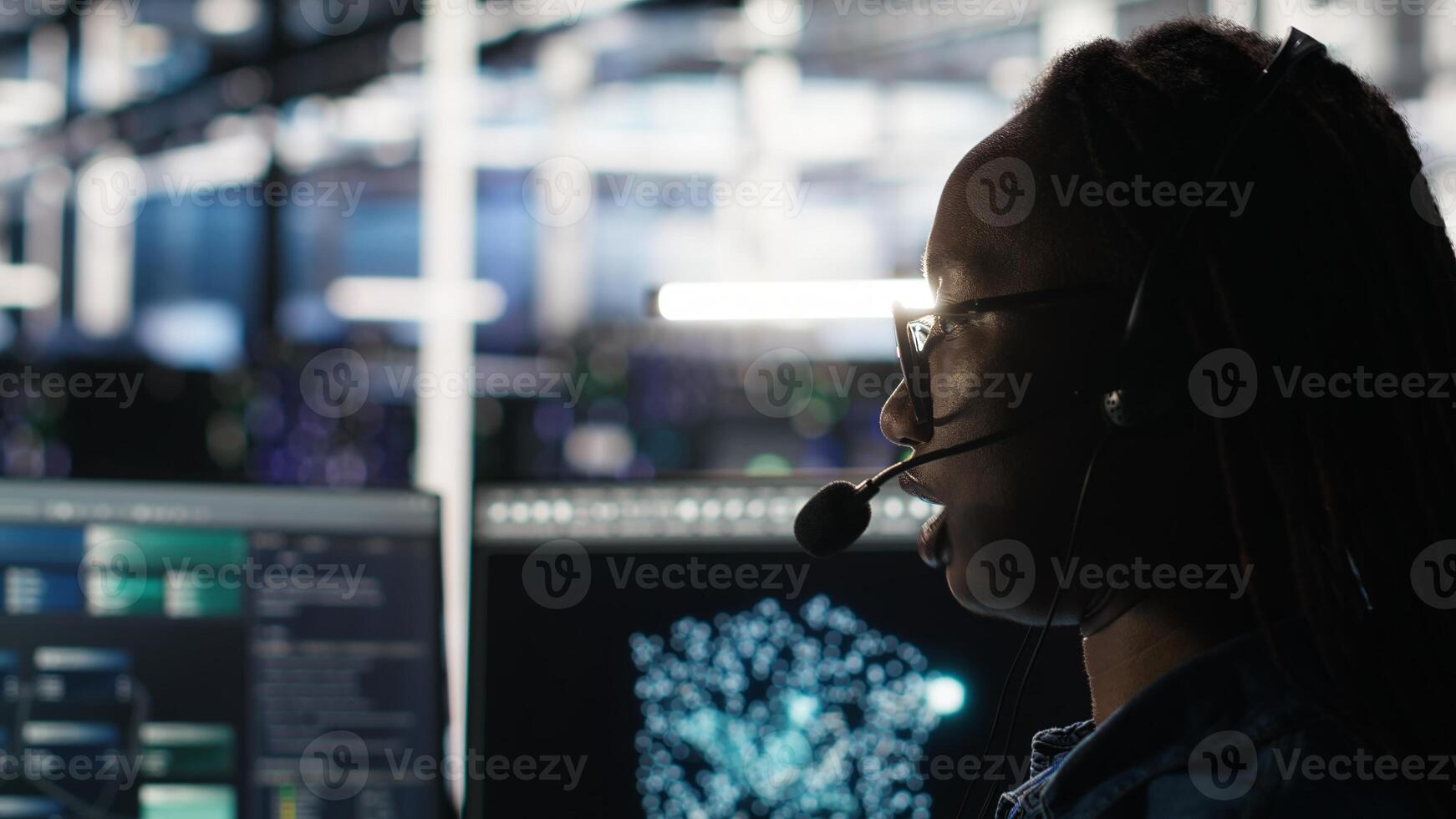 Data center employee uses audio headset and visual programming dashboard to troubleshoot client reported issues. Server farm technician looks at node tree interface, talking in microphone photo