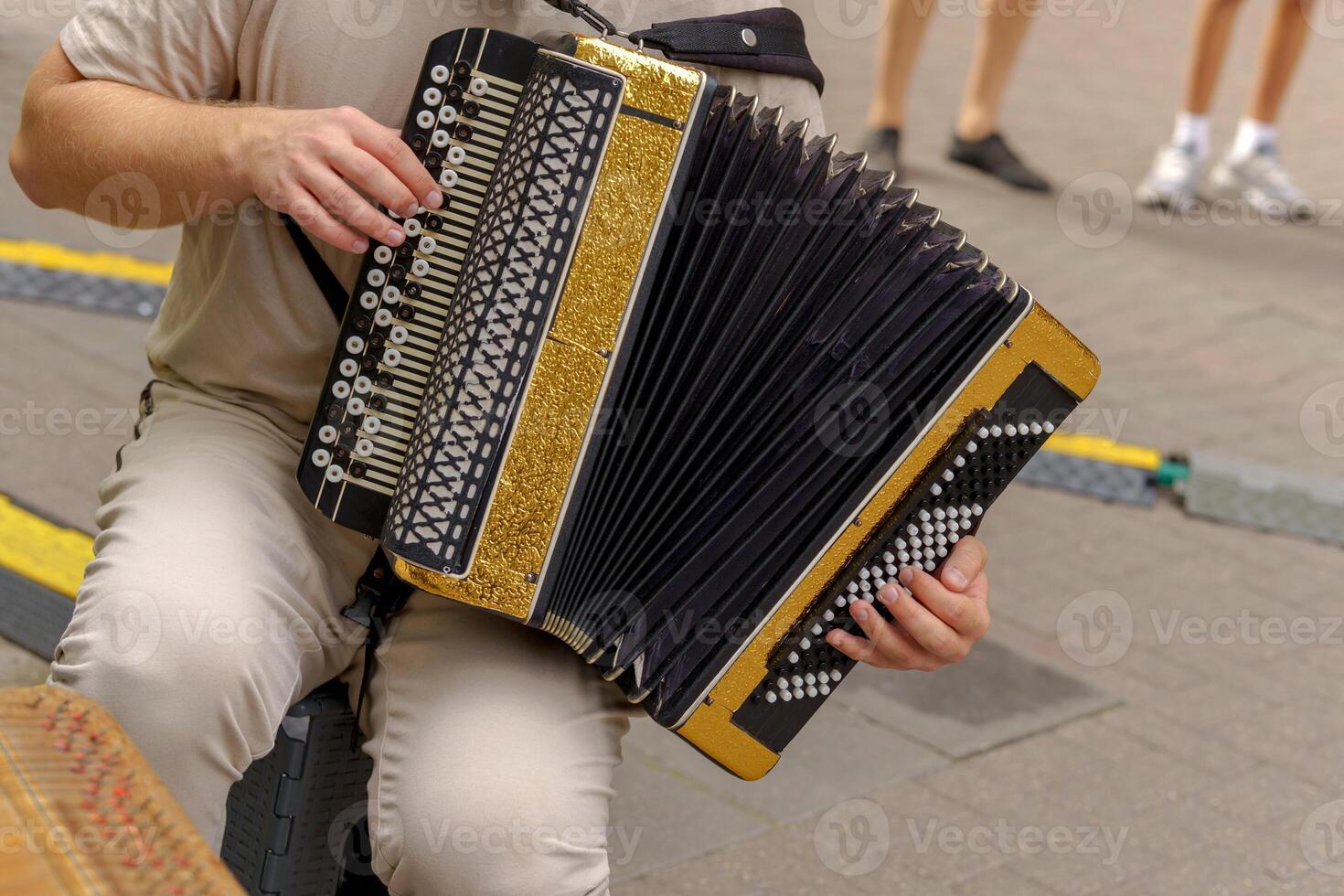 A gold and black accordion with ornate details rests on the lap of a seated player. Its glossy surface and intricate buttons highlight the craftsmanship of the instrument. photo