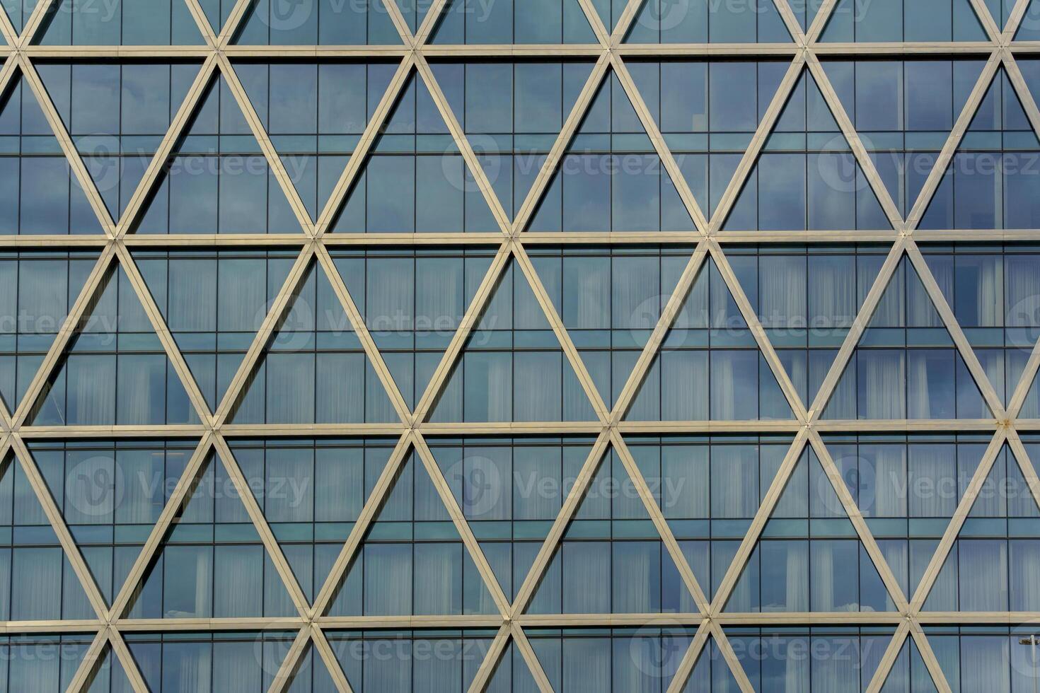 A building facade features a repeating pattern of triangular metal beams filled with reflective glass. The modern lattice design combines structural precision with visual rhythm. photo