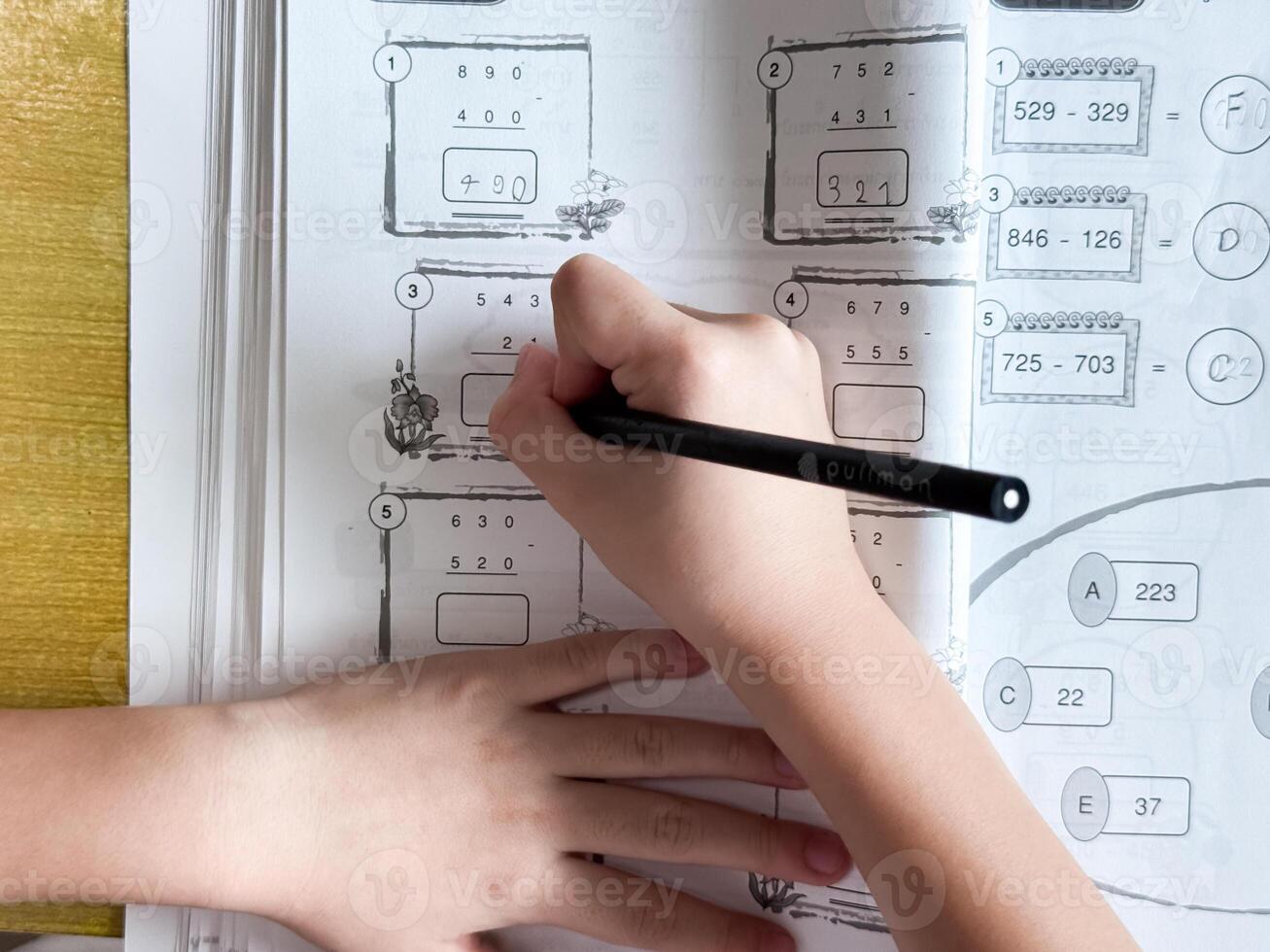 A young student sits at a wooden desk working on basic math exercises, steadily developing essential problem solving skills.o photo
