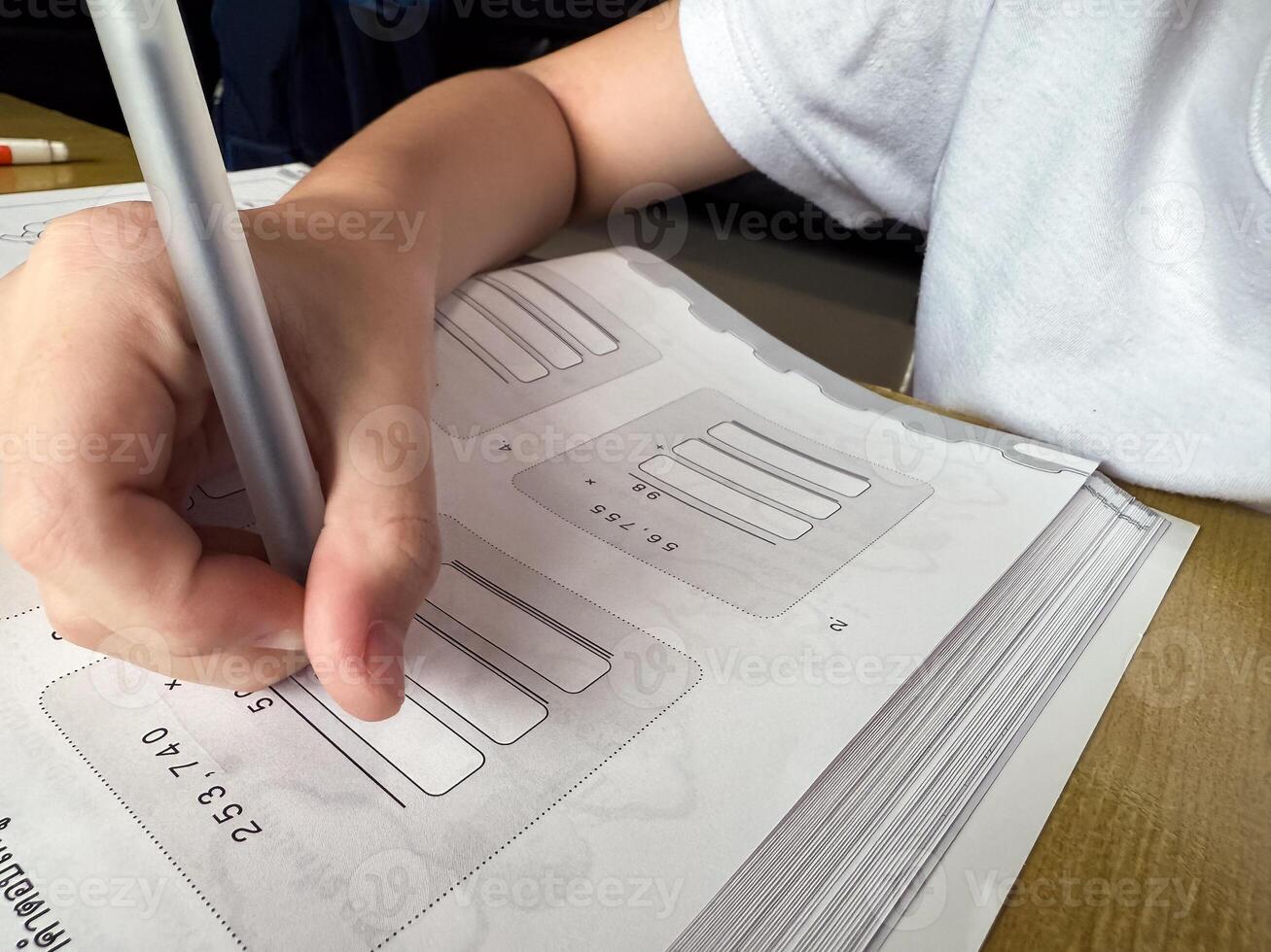 A young student sits at a wooden desk working on basic math exercises, steadily developing essential problem solving skills.f photo