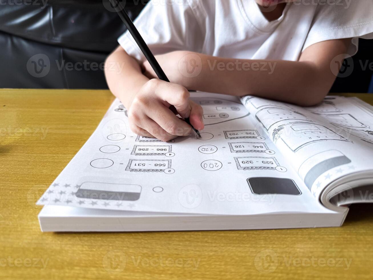 A young student sits at a wooden desk working on basic math exercises, steadily developing essential problem solving skills. a photo