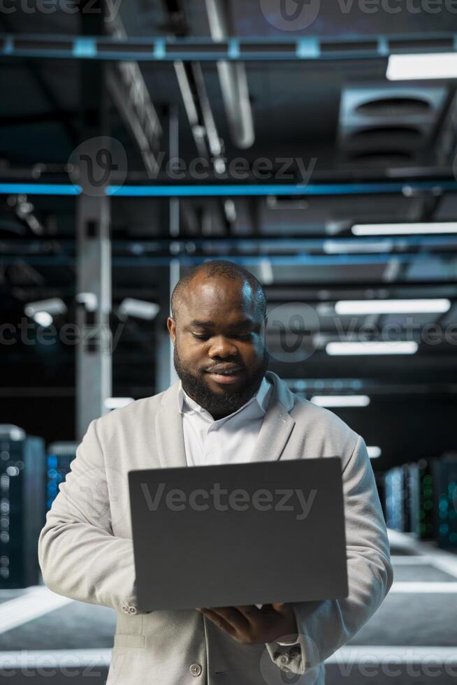 Engineer in server farm managing infrastructure systems, checking recovery plan on laptop. Data center worker monitoring performance using automation tools, making sure rigs are functioning optimally photo