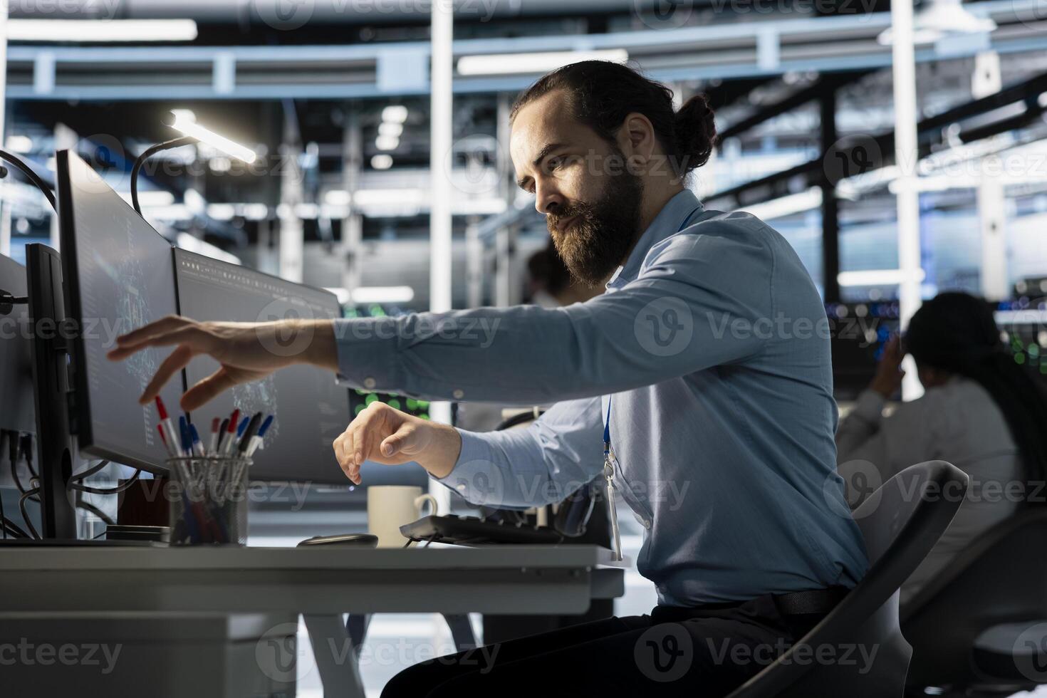 Engineer in data center using PC to update storage arrays software, configuring network virtualization. Man in server room using computer to verify settings, maintaining stable performance photo