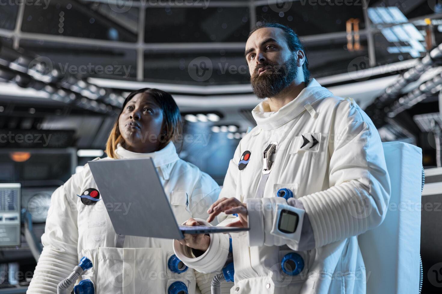 Team of astronauts in spacecraft using laptop to run telemetry data analysis. Teamworking spaceship crew colleagues in spacesuits analyzing mission logs on notebook during planetary exploration photo