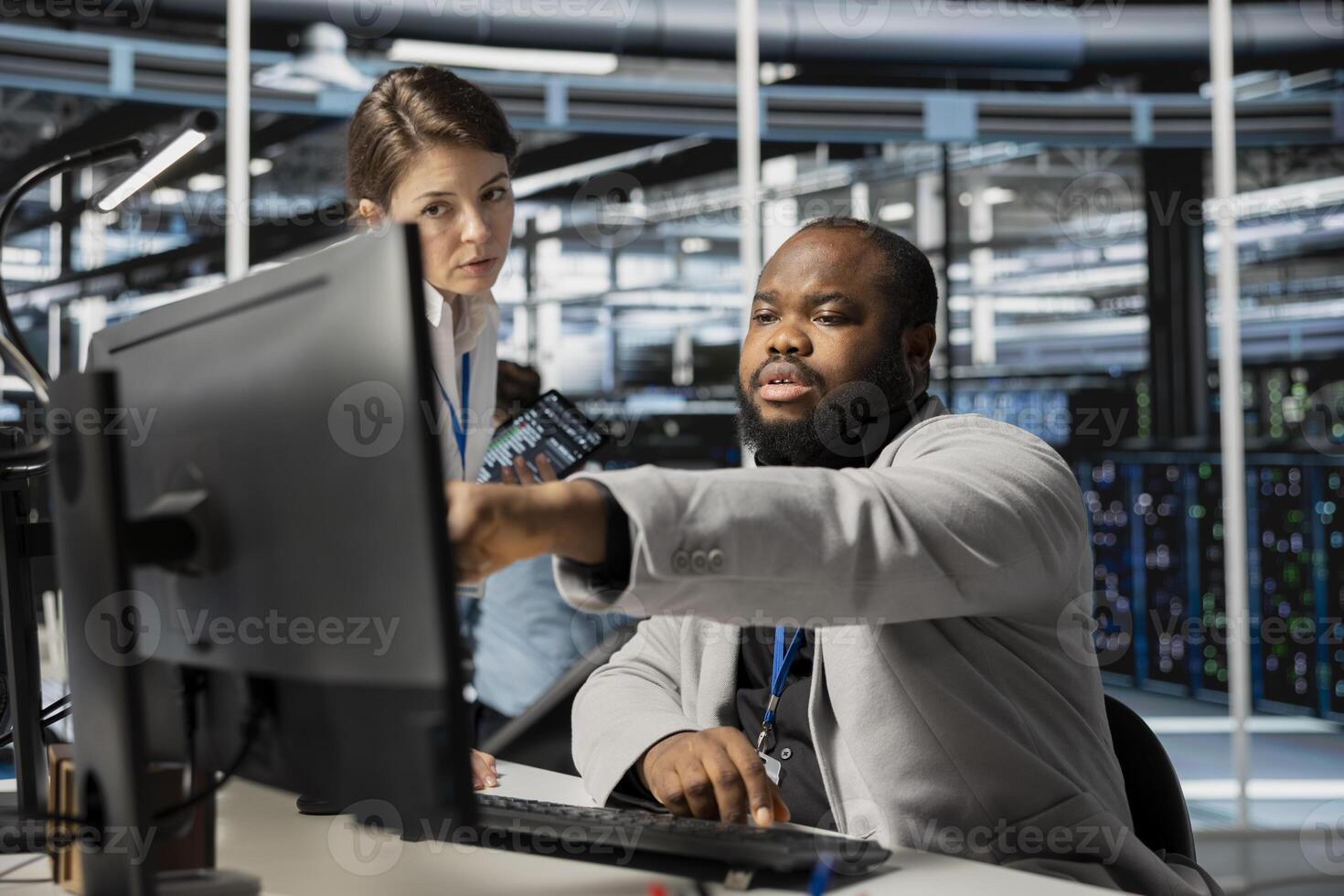 Data center manager supervising engineer running diagnostic scripts on computer, examining gear. Server room supervisor overseeing worker using PC to evaluate rackmounts performance metrics photo
