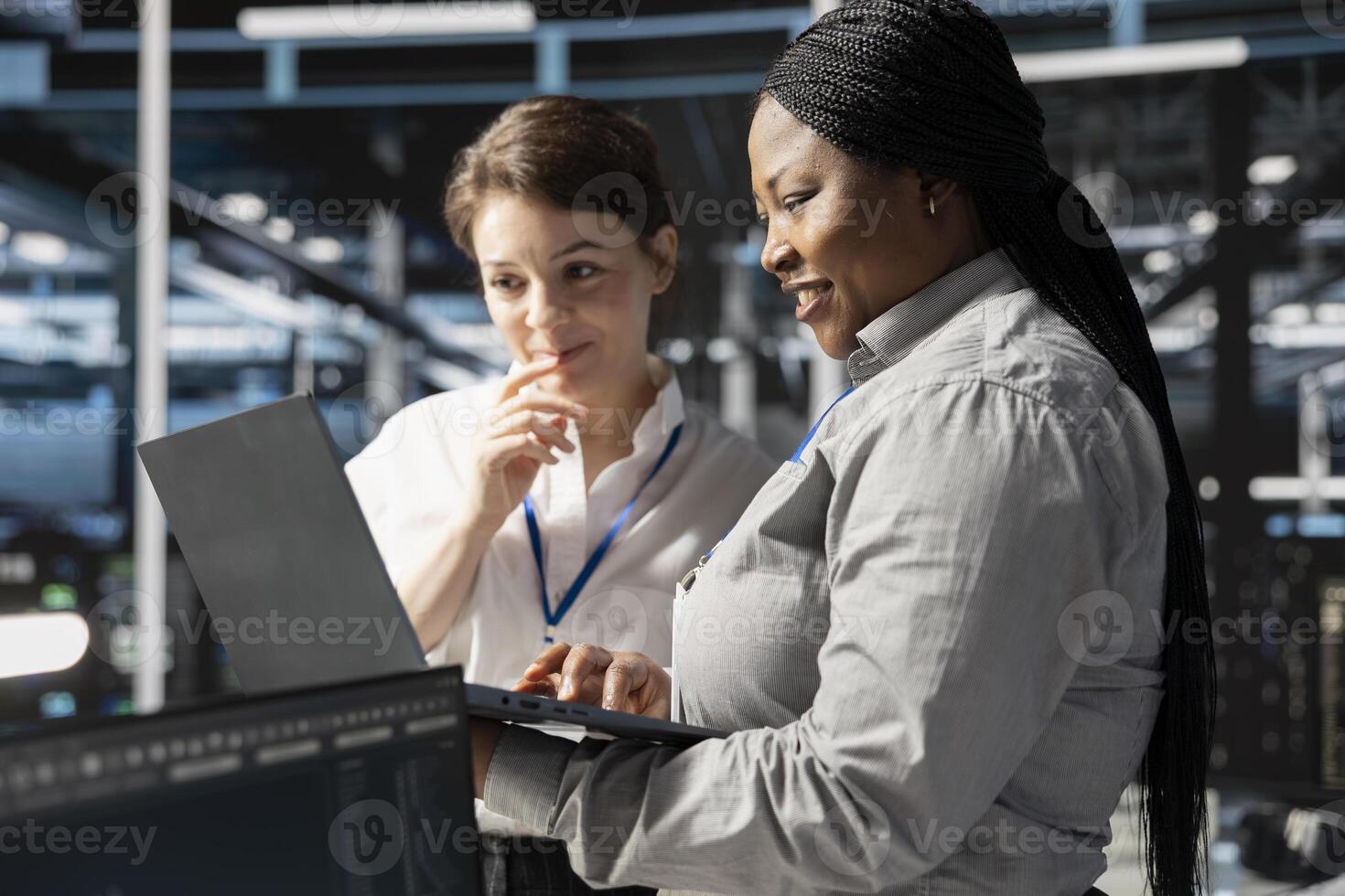 Smiling engineering team using laptop in data center, managing server virtualization, running scripts. Happy coworkers using programming language on notebook in server farm photo