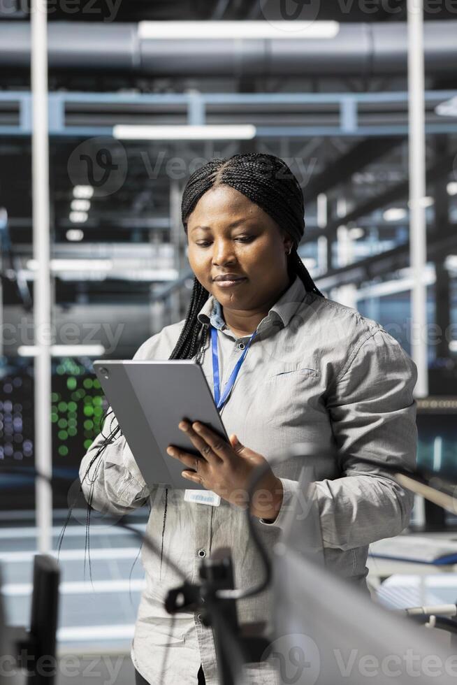 Woman in data center doing software updates, verifying deep learning parameters. African american server hub IT expert using PC to inspect configurations, ensuring optimal application performance photo