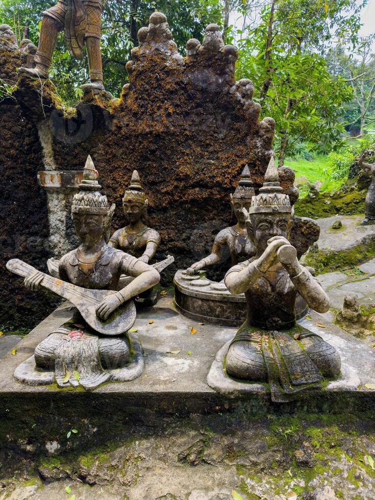 A close-up, medium-shot view of ancient stone statues of mythical musicians, one playing a stringed instrument and another holding a flute-like object, situated in a lush, moss-covered garden photo