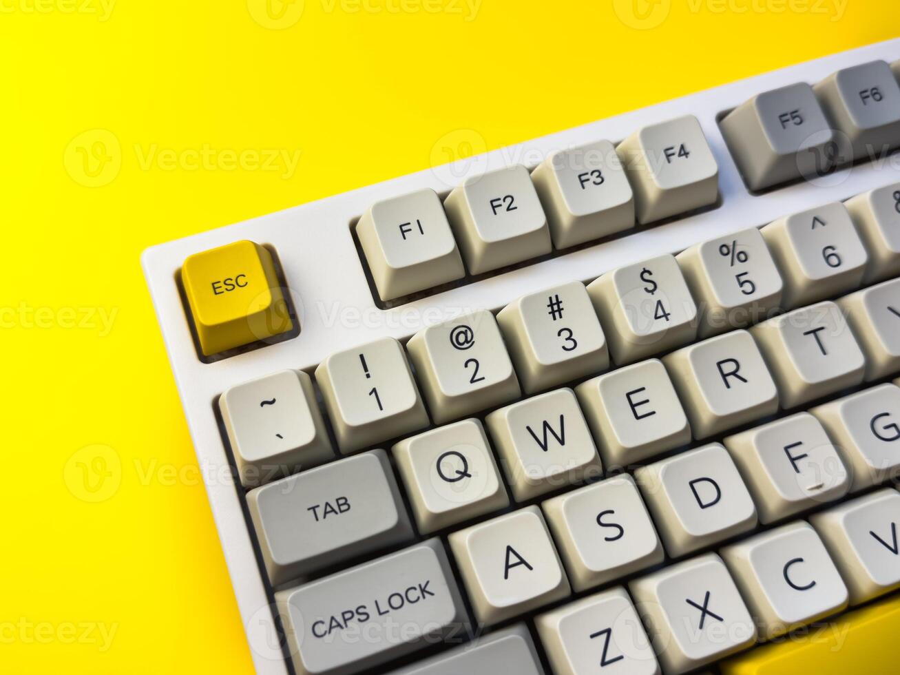 White keyboard with Esc key on bright yellow background, minimalism, keyboard buttons. A keyboard with a yellow key on the bottom left photo