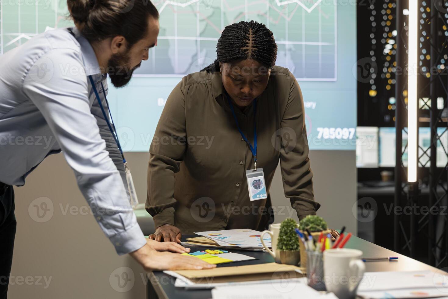 Multiethnic team reviewing analytics in a late night company briefing after hours, leveraging projections and data insights to align business goals with expectations in a modern office space. photo